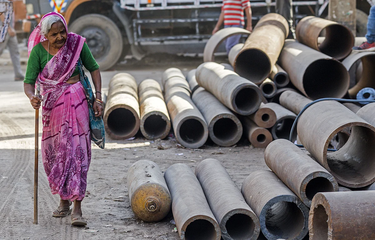 An elderly woman walks past metal pipes on a street in New Delhi. (Photographer: Prashanth Vishwanathan/Bloomberg)