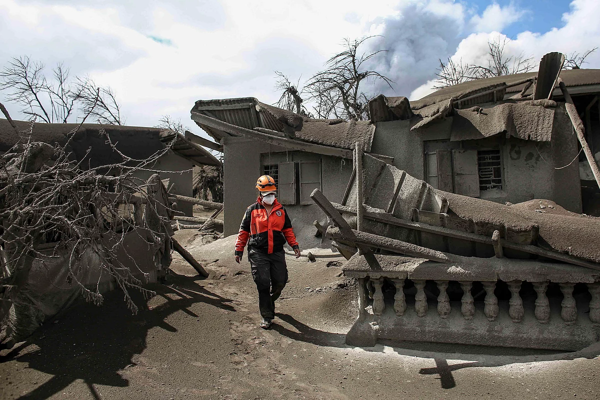 In this Jan. 14, 2020, photo, a rescue volunteer walk on the Taal volcano island beside damaged structures men in Talisay, Batangas province, southern Philippines, as Taal volcano continues to spew ash. The volcano near the Philippine capital spewed lava into the sky and trembled constantly Tuesday, possibly portending a bigger and more dangerous eruption, as tens of thousands of people fled villages darkened and blanketed by heavy ash. (Source: AP Via PTI)