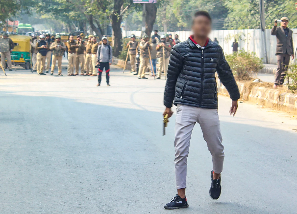 A person (face blurred as his being an adult could not be ascertained), brandishes a gun towards people protesting against the Citizenship Amendment Act, near Jamia Millia Islamia University, in New Delhi, Thursday, Jan. 30, 2020. (Source: PTI)