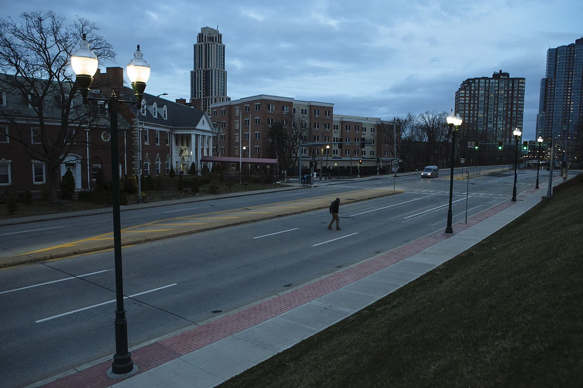 A pedestrian crosses an empty street in New Rochelle, New York, U.S., on Monday, March 16, 2020. The governors of New York, New Jersey and Connecticut banned all gatherings of 50 or more people, and said bars, restaurants, casinos and gyms must close Monday at 8 p.m. (Photographer: Angus Mordant/Bloomberg)