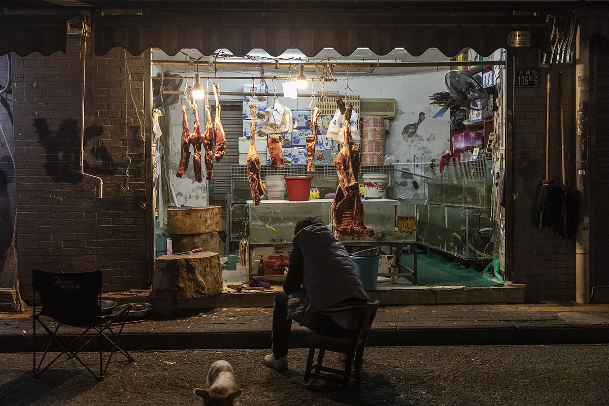 A man sits in front of a butcher’s store in Wuhan, China, on Dec. 9, 2019. (Photographer: Qilai Shen/Bloomberg)