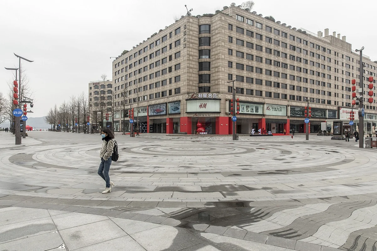 A pedestrian wearing a face mask walks through an empty shopping plaza, in view of a Hennes & Mauritz AB (H&M) store, in Hangzhou, China, on Tuesday, Feb. 11, 2020. (Photographer: Qilai Shen/Bloomberg)