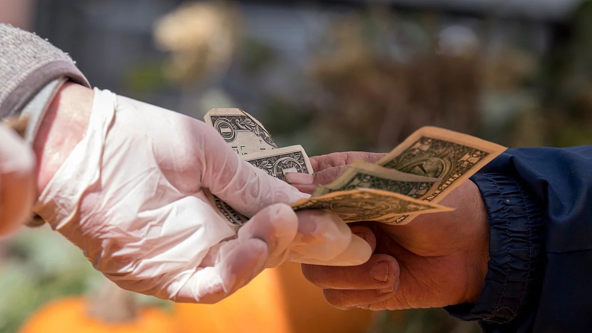 A shopper pays for a purchase with cash at a farmers market. (Photographer: David Paul Morris/Bloomberg)
