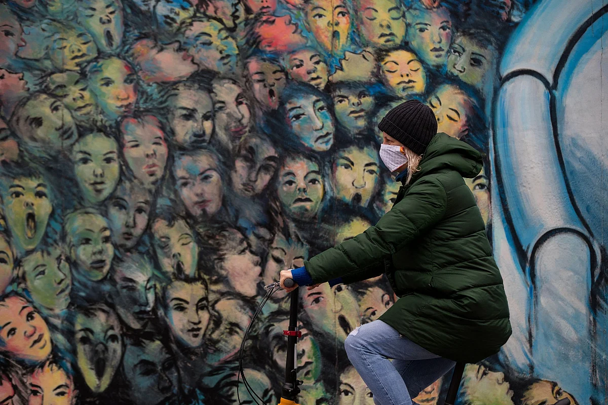 A cyclist wearing a protective face mask passes the Berlin Wall East Side Gallery, on Monday, April 13, 2020. (Photographer: Krisztian Bocsi/Bloomberg)