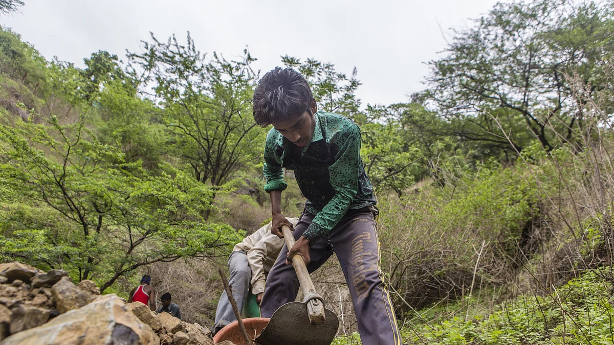 A worker uses a shovel to place boulders in a bowl while building a stone dam as part of a project to stop rainwater flows in Dewas, Madhya Pradesh, India (Photographer: Prashanth Vishwanathan/Bloomberg)