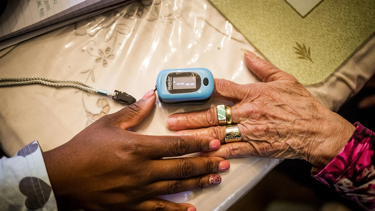 A nurse uses a pulse oximeter on a lady at her home. (Photographer: John Taggart/Bloomberg).