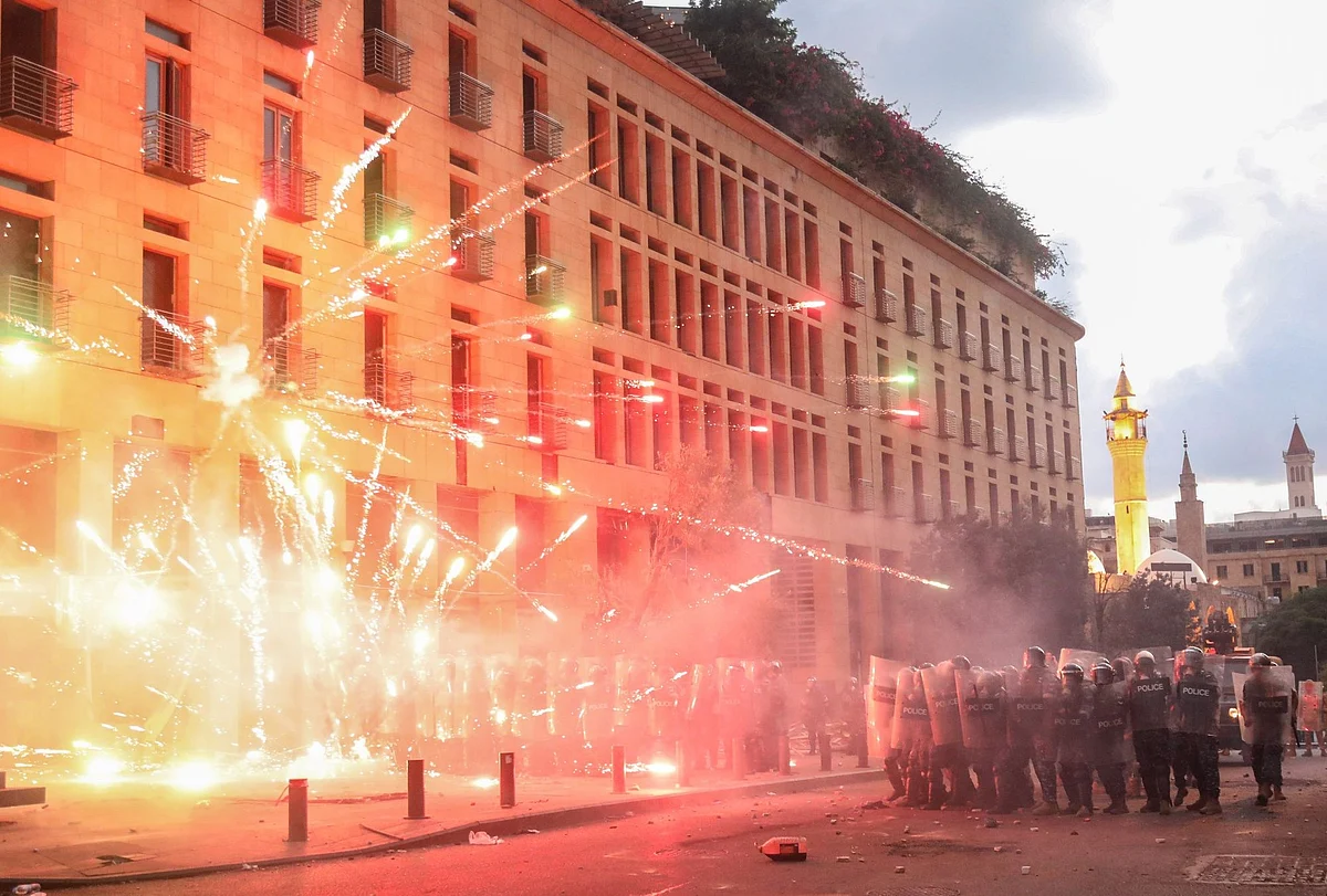 Fireworks explode near riot police during a protest in Beirut on Aug. 10. The Lebanese government resigned after a massive explosion of improperly stored ammonium nitrate in the city’s port rocked the capital, killing hundreds and injuring thousands. Photographer: Hasan Shaaban/Bloomberg 