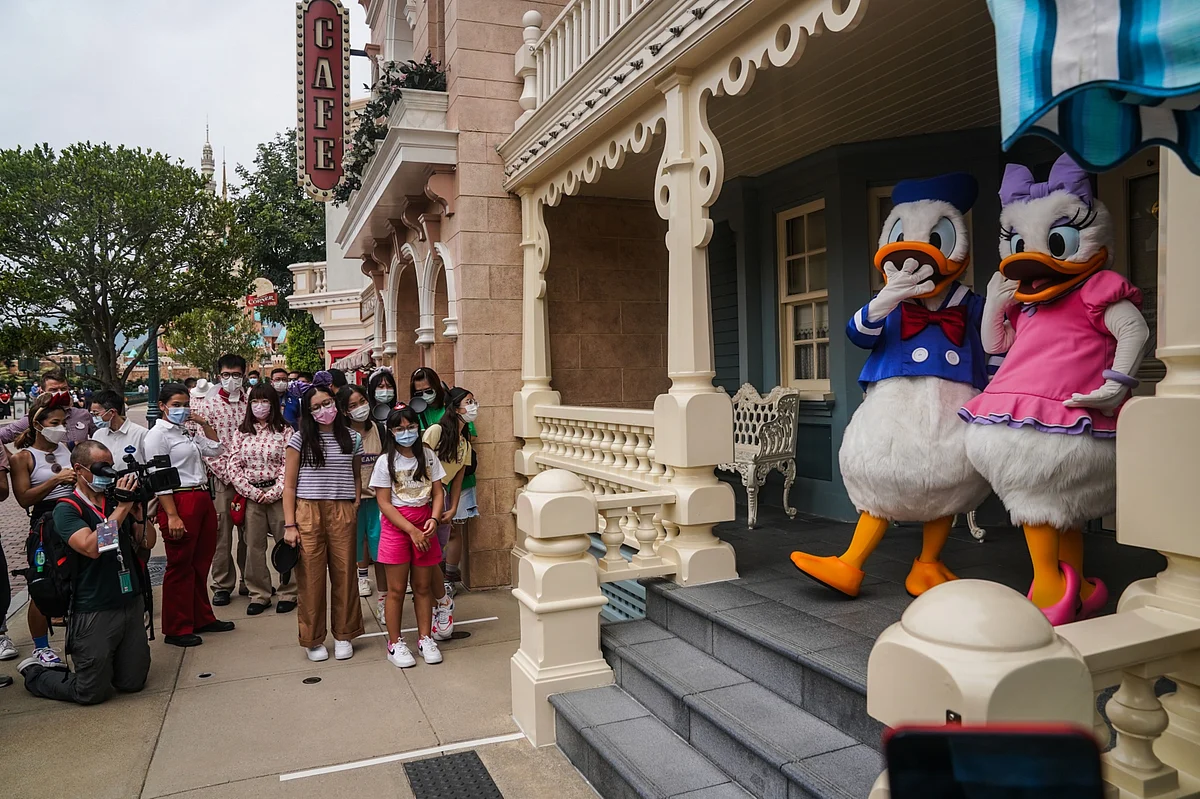 Visitors wearing protective masks watch actors dressed up as Donald Duck and Daisy Duck at the Disneyland Resort, in Hong Kong, on Sept. 25, 2020. (Photographer: Lam Yik/Bloomberg)