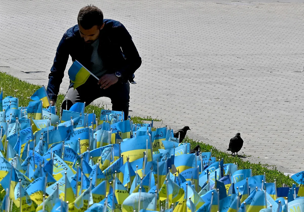 A man sticks into a grass plot small Ukrainian flags carrying the names of the Ukrainian servicemen killed in the war with Russia, in the center of Ukrainian capital of Kyiv on June 22, 2022. Photographer: Sergei Supinsky/AFP/Getty Images