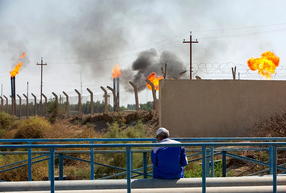 A man sits across flare stacks burning off excess gas at the Nahr Bin Omar oilfield in Iraq's southern province of Basra. Photographer: Hussein Faleh/AFP/Getty Images