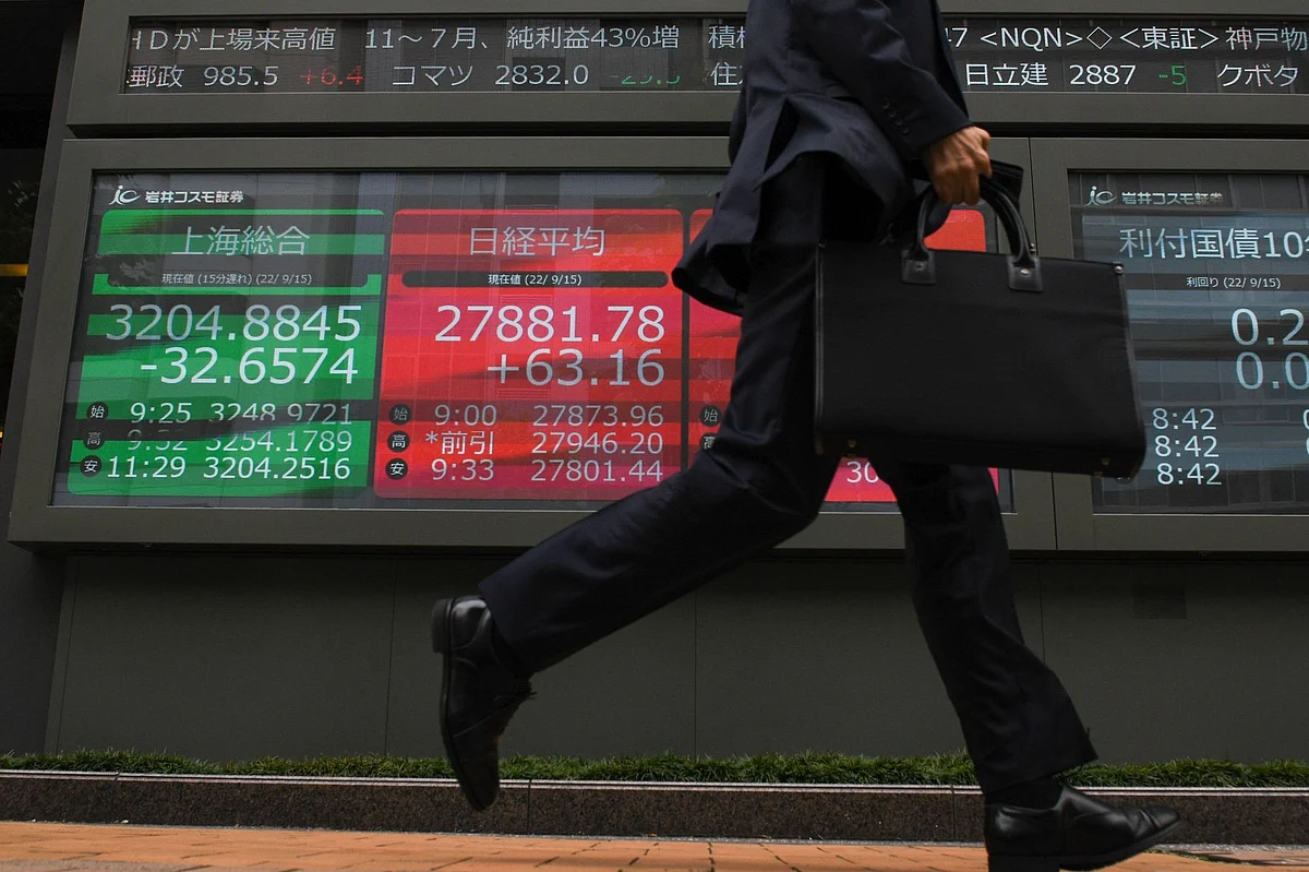 A pedestrian in front of an electronic stock board displaying the Shanghai Composite Index, left, and the Nikkei 225 Stock Average figures, middle, outside a securities firm in Tokyo, Japan, on Thursday, Sept. 15, 2022. Photographer: Noriko Hayashi/Bloomberg