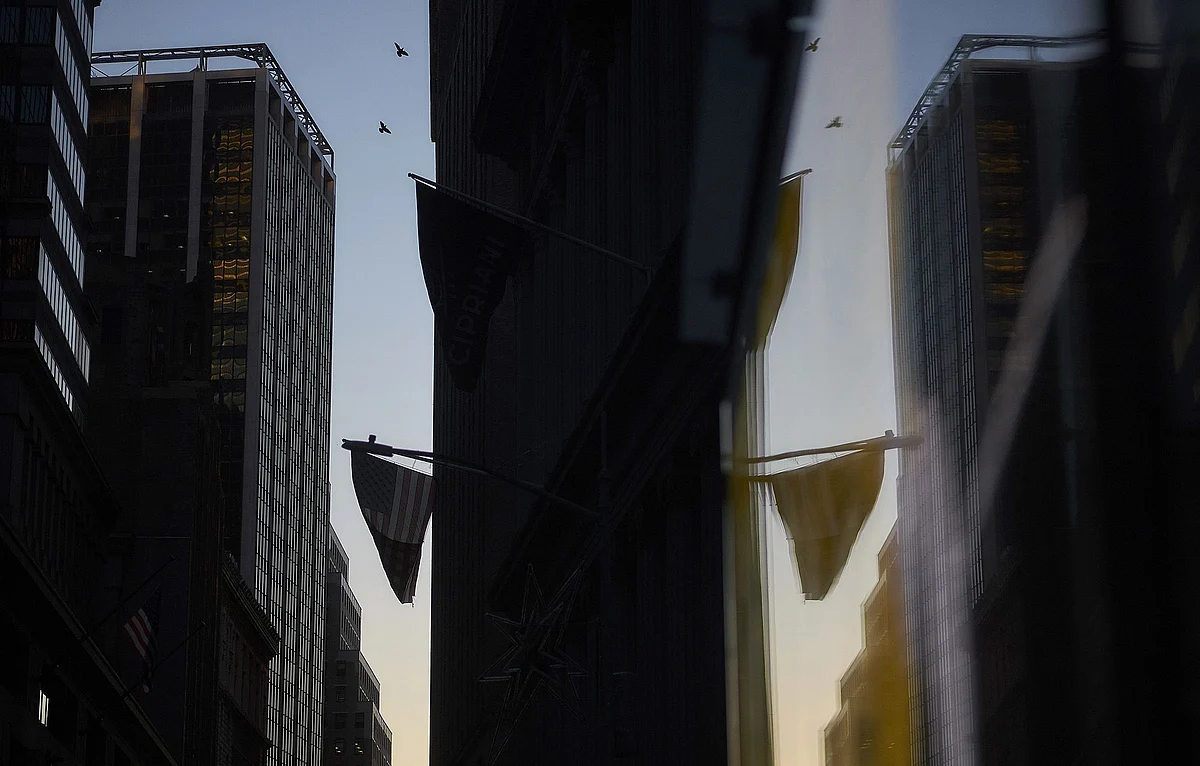 An American flag is reflected in the window of a building near the New York Stock Exchange. Photographer: John Taggart/Bloomberg