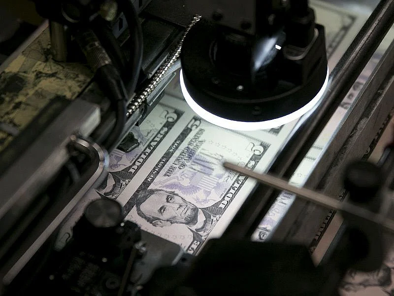 Sheets of five dollar notes go through a machine to receive a serial number and the seals of the U.S. Treasury and Federal Reserve at the Bureau of Engraving and Printing in Washington, D.C., U.S., on Tuesday, April 23, 2013. Photographer: Andrew Harrer/Bloomberg