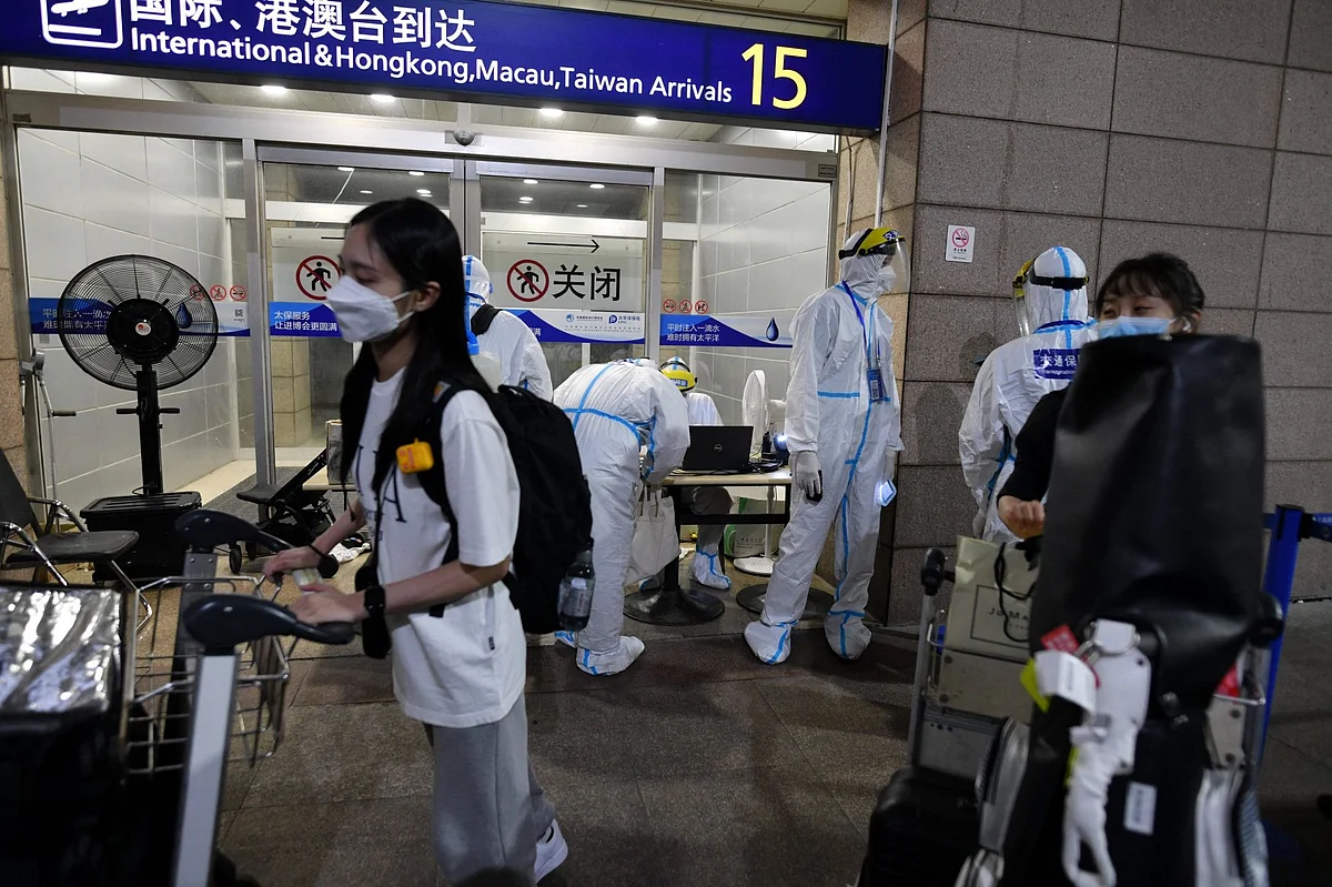 Workers in protective clothing helps arriving international passengers as they prepare to board buses to be taken to quarantine hotels, at Pudong airport in Shanghai on August 13. Photographer: Greg Baker/AFP/Getty Images