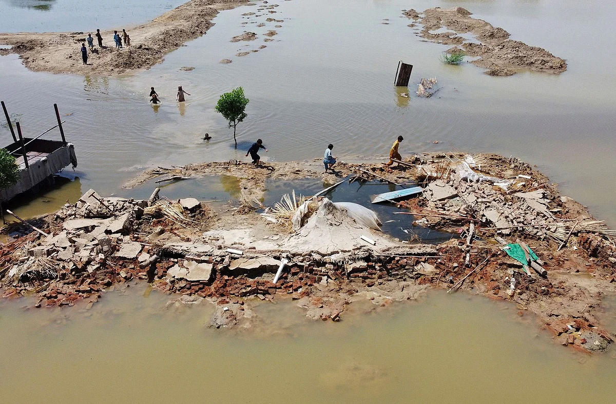 Flood-affected people wading next to a house that collapsed after heavy monsoon rains in Jaffarabad district of Balochistan province, Pakistan on on Aug. 31, 2022. Photographer: Fida Hussain/AFP/Getty Images
