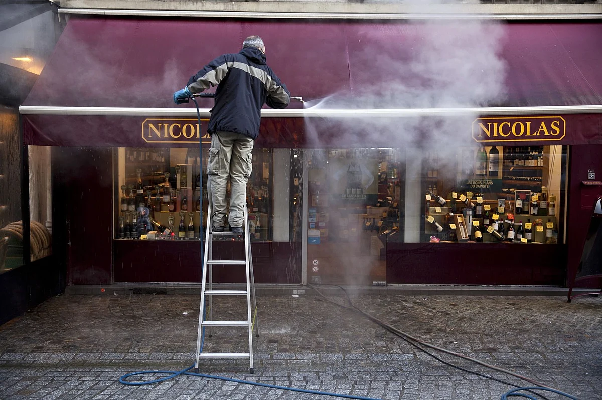 A worker cleans the awning of a Castel Freres Nicolas store in Paris. Photographer: Balint Porneczi/Bloomberg
