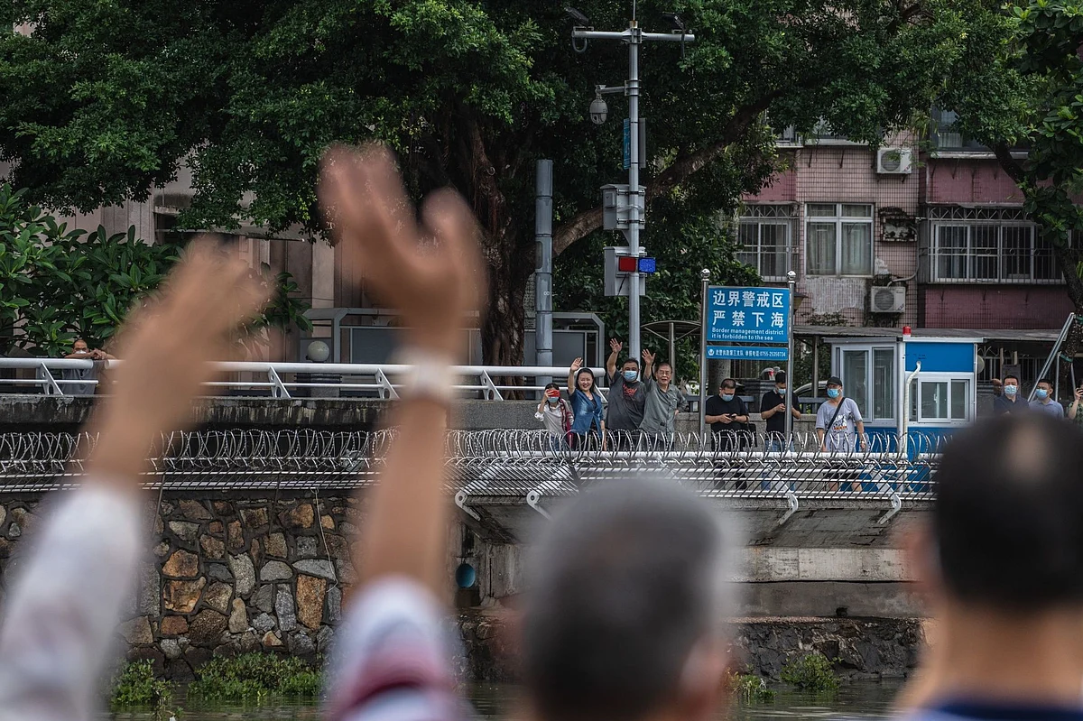 People in mainland China, back, wave across the border toward the closed town of Sha Tau Kok in Hong Kong, in June 2022.