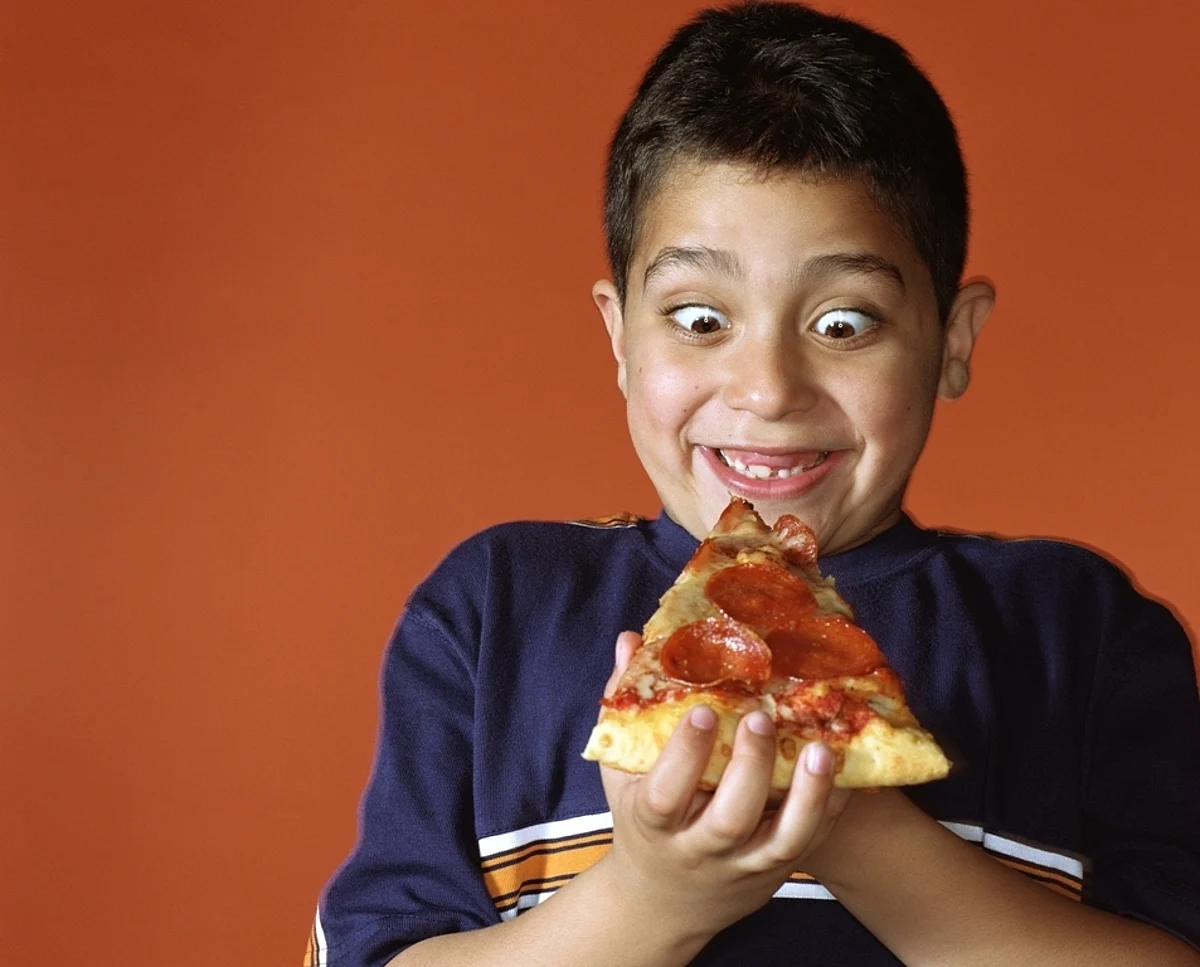 Boy (7-9) smiling while looking down at slice of pepperoni pizza