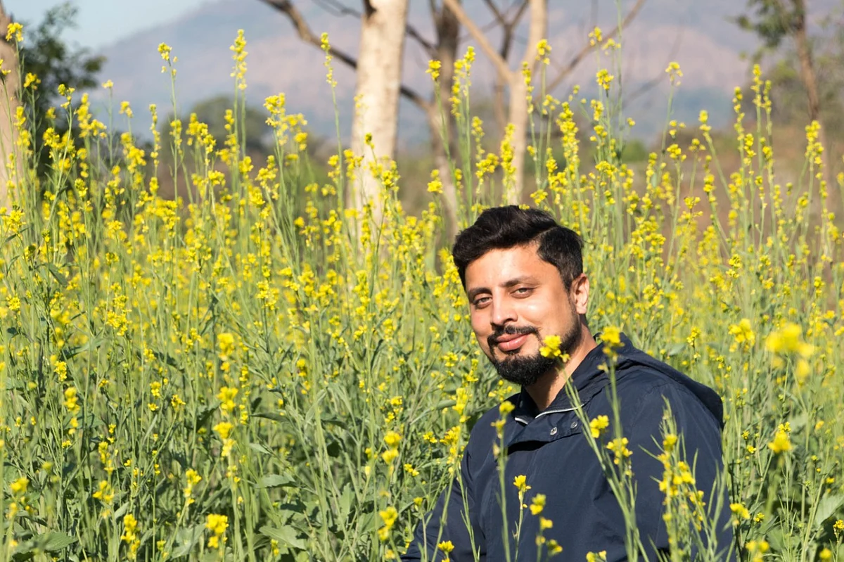 Bee man Amit Godse amid a field of yellow flowers