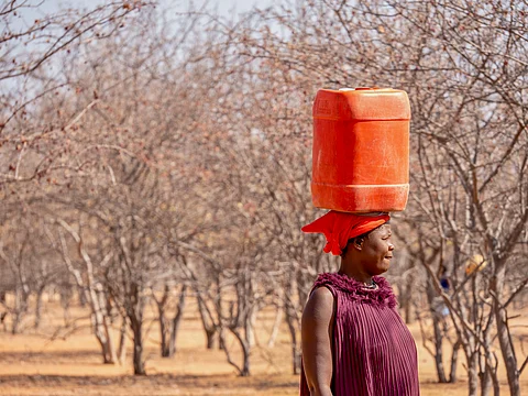 An African woman walking back to her rural village, carrying a jerry can of drinking water on her head. 