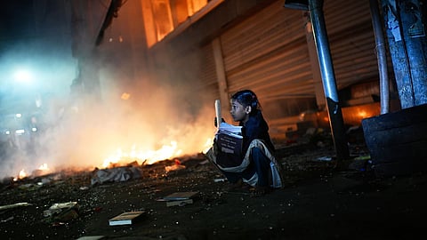 A girl rescues books from a shop near the premises of the Prothom Alo daily newspaper which was set on fire by angry protesters after news reached the country from Singapore of the death of a prominent activist Sharif Osman Hadi, in Dhaka, Bangladesh, Friday, Dec. 19, 2025. 