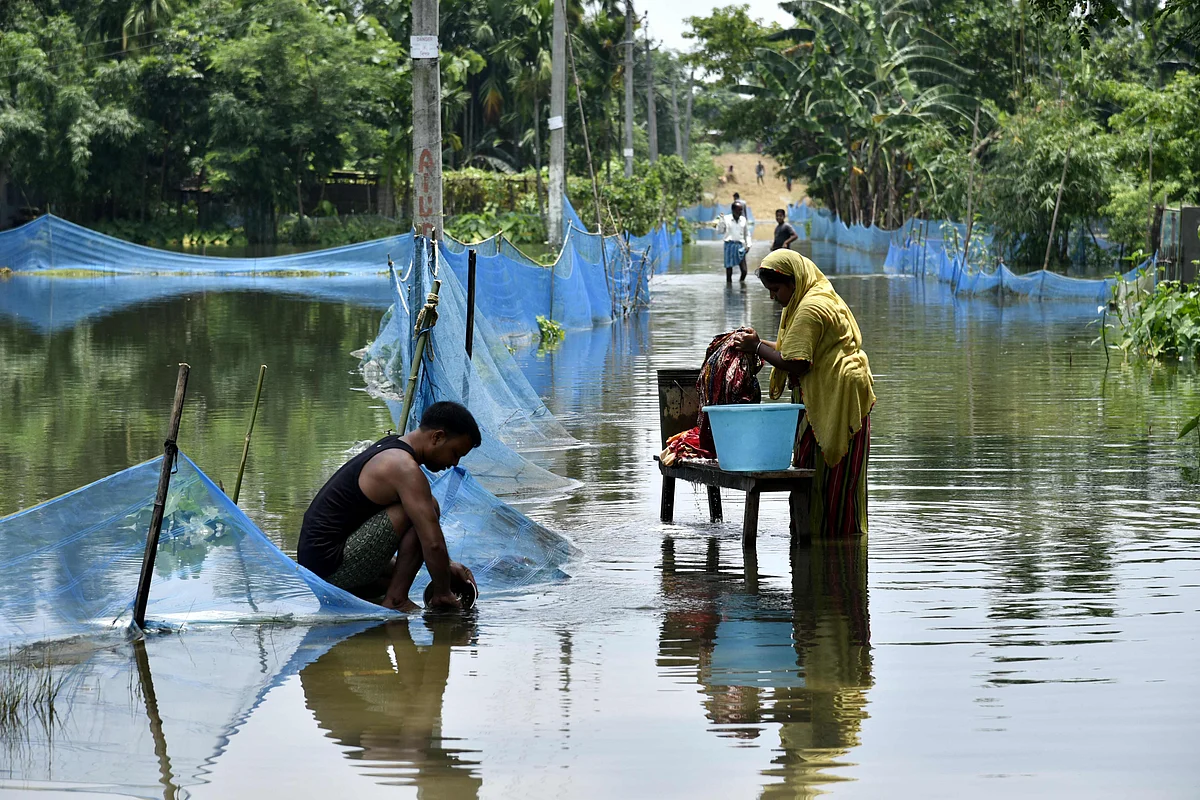 An Indian woman washes clothes next to man cleaning a pot along a flooded road following heavy monsoon rains at Kaljhar village in Barpeta district of Assam