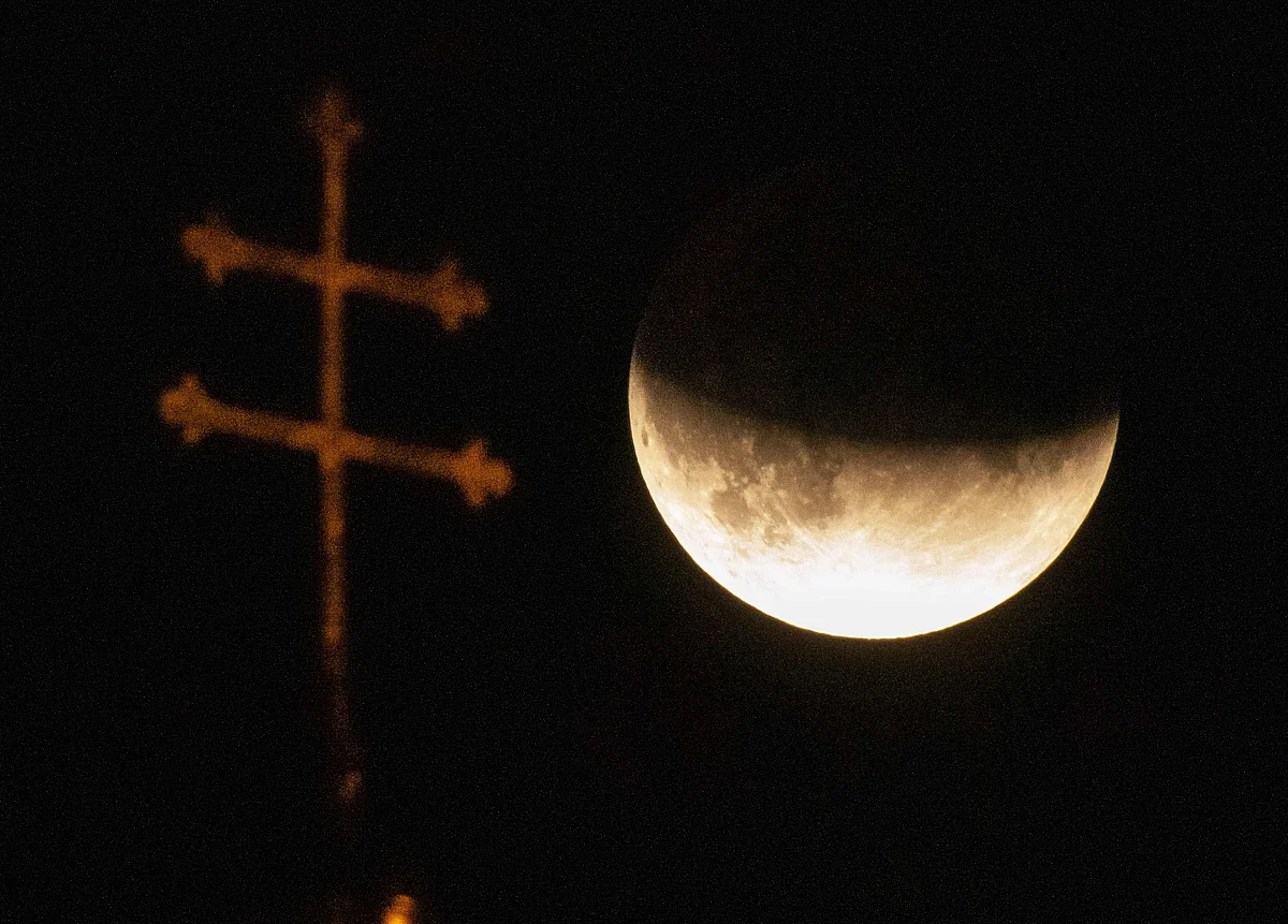 The cross of a church is pictured in front of the moon during a partial lunar eclipse in Munich, Germany, on July 16, 2019.