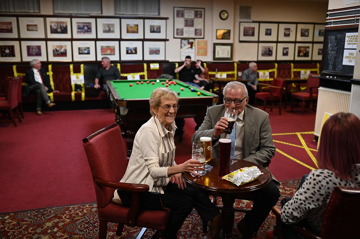 People enjoy a drink with yellow tape on the seats and floor aiding social distancing inside the Burnley Miners Working Mens Social Club in Burnley, northwest England, on July 4, 2020, as restrictions are further eased during the novel coronavirus COVID-19 pandemic.