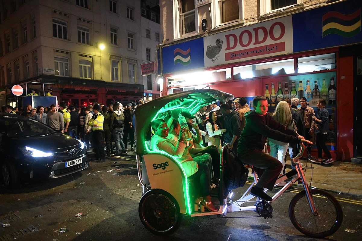 A woman in a pedicab smiles as she is conveyed through streets filled with revellers outside the bars in the Soho area of London on July 4, 2020, following a further easing of restrictions to allow pubs and restaurants to open during the novel coronavirus COVID-19 pandemic