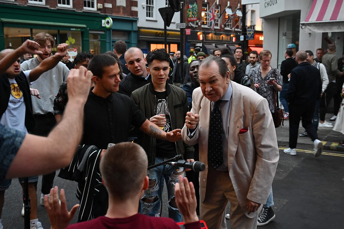 A man (C) drinks a shot of whisky in the street in the Soho area of London on July 4, 2020, as restrictions are further eased during the novel coronavirus COVID-19 pandemic.