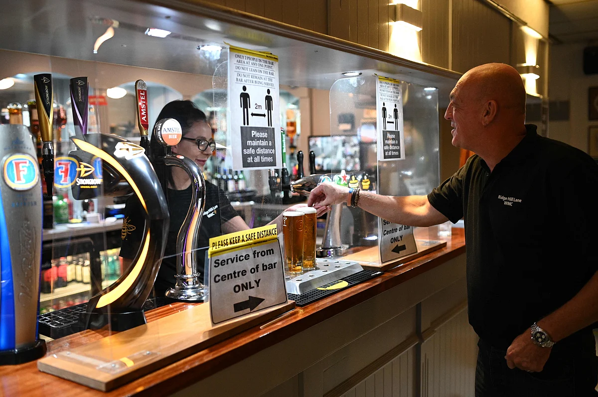 A man pays for drinks at a bar protected by a perspex screen with signs reminding members to socially distance inside the Ridge Hill Working Mens Club in Stalybridge, northwest England, on July 4, 2020, as restrictions are further eased during the novel coronavirus COVID-19 pandemic.