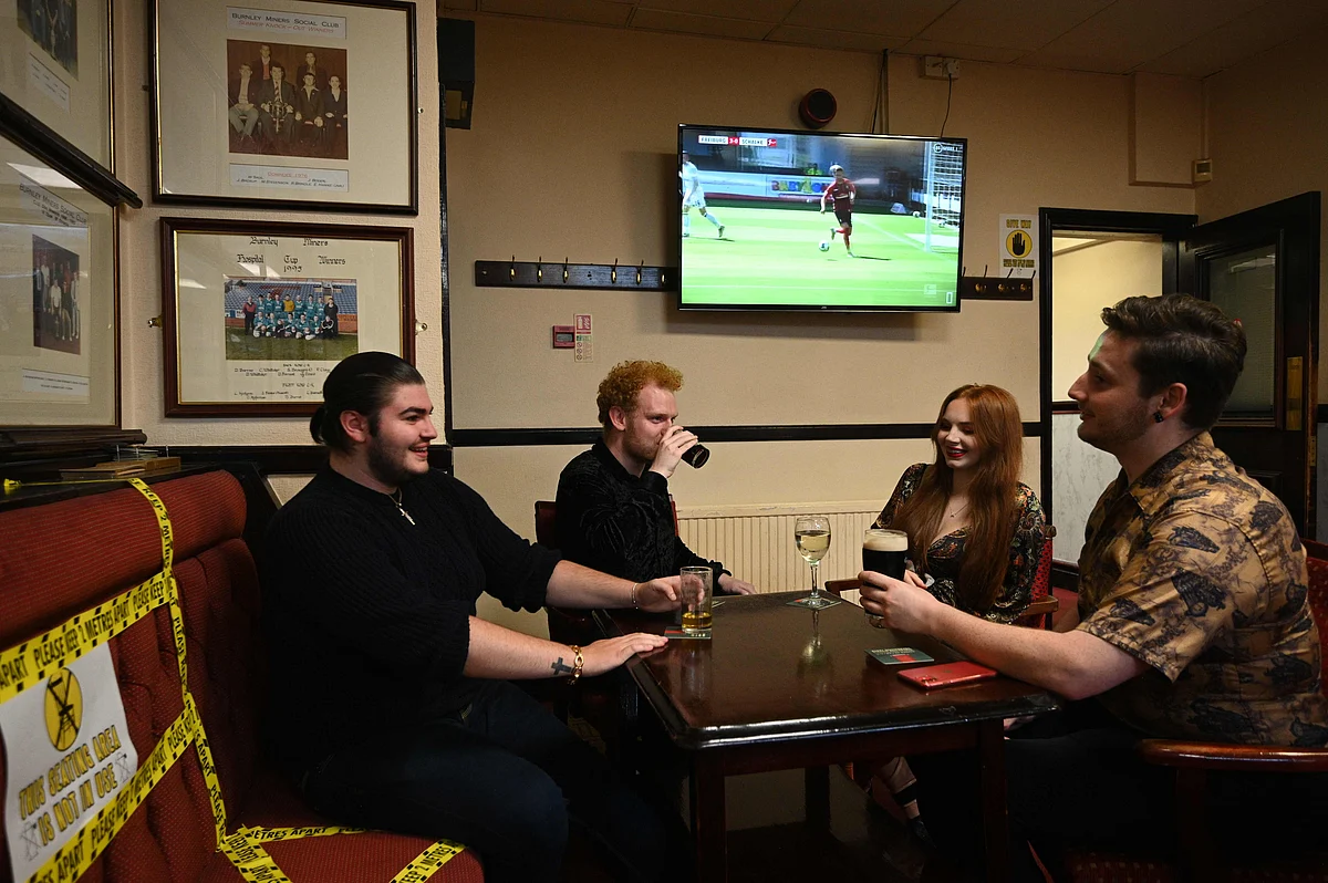 People enjoy a drink with yellow tape on the seats and floor aiding social distancing inside the Burnley Miners Working Mens Social Club in Burnley, northwest England, on July 4, 2020, as restrictions are further eased during the novel coronavirus COVID-19 pandemic.
