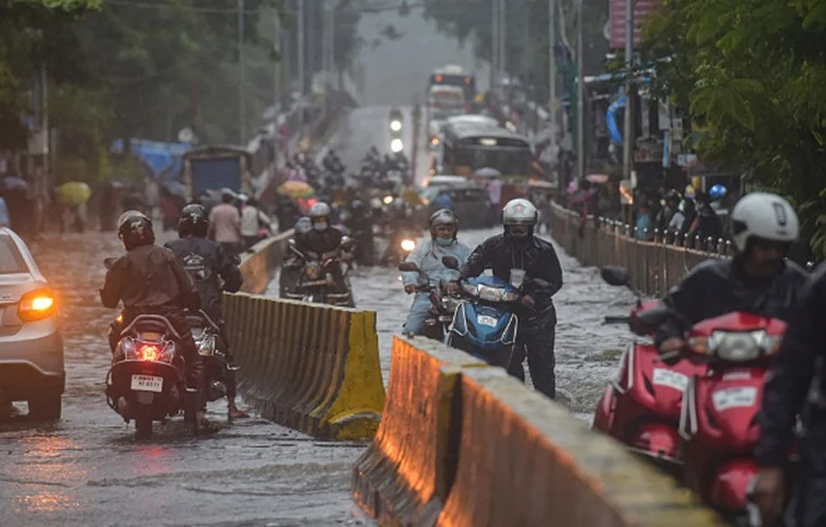Commuters make way through a waterlogged road during rain, in Mumbai, Wednesday, Aug