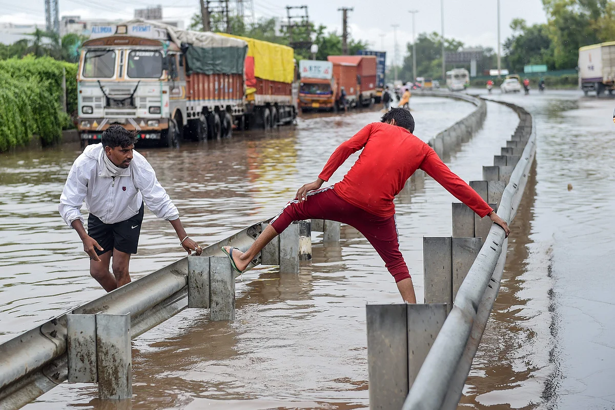 People cross a flooded road on a highway following monsoon rainfall in Gurugram on August 20, 2020.
