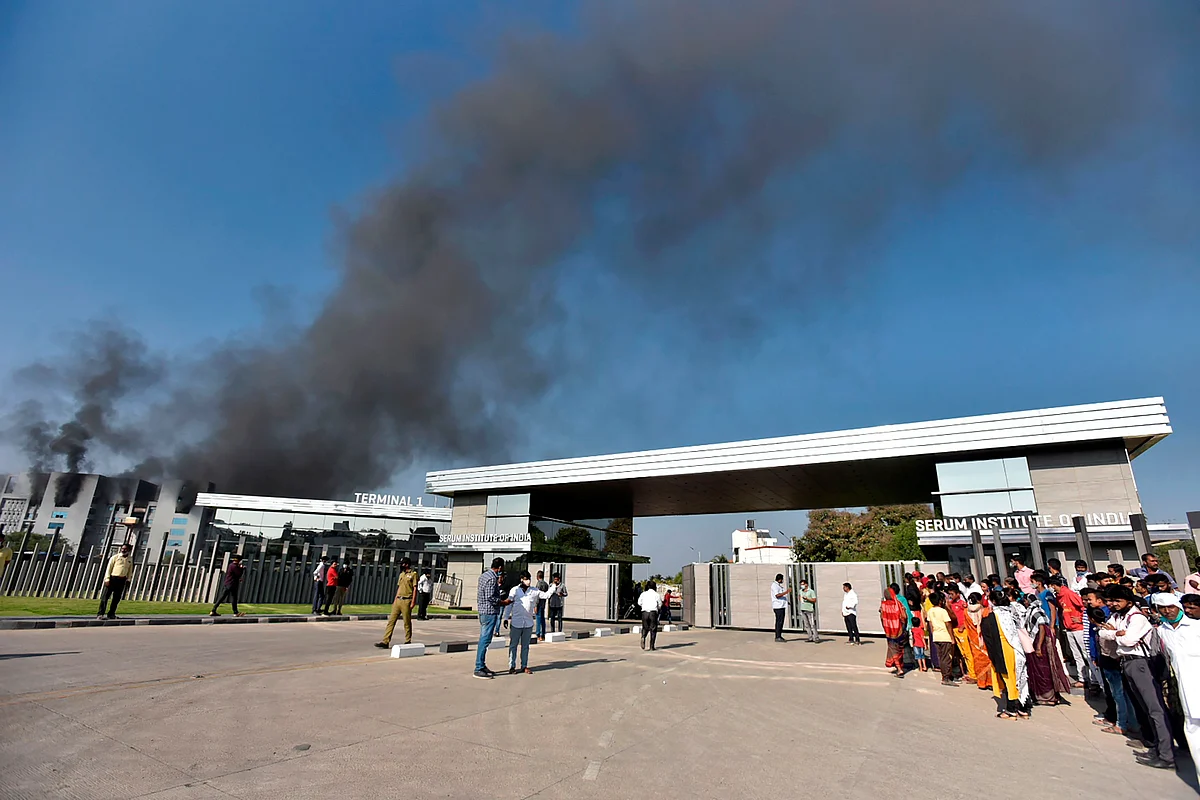 People stand as smoke rises after a fire broke out at Indias Serum Institute in Pune on January 21, 2021. - A fire broke out on January 21 at Indias Serum Institute, the worlds largest maker of vaccines, but a company source said production of drugs to prevent Covid-19 coronavirus was not affected