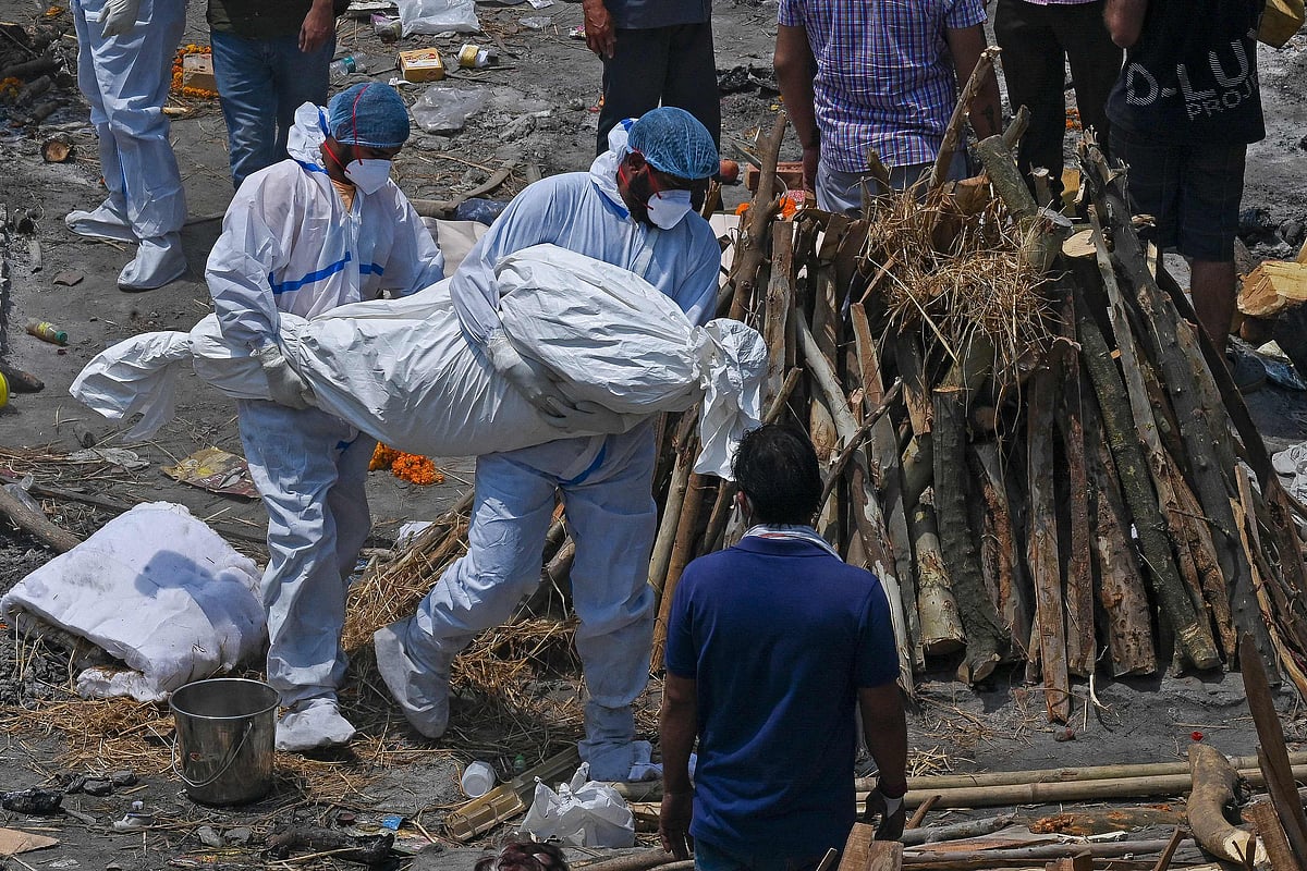Family members and ambulance worker wearing PPE kit (Personal Protection Equipment) carry the bodies of the patients who died of the Covid-19 coronavirus at a cremation ground in New Delhi on April 27, 2021.