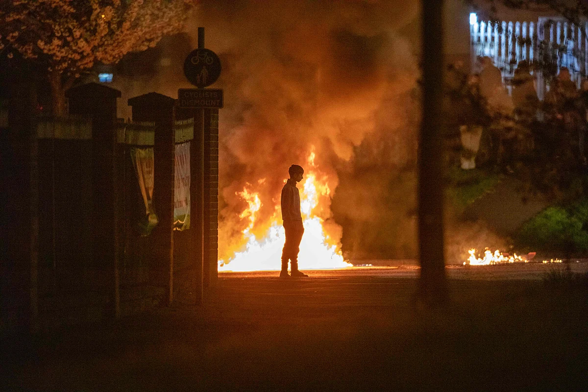 A boy stands and looks on as flames and smoke rises behind him at the scene of violence in Newtownabbey, north of Belfast, in Northern Ireland on April 3, 2021.