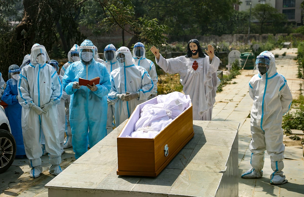 A priest reads the bible during the last rites of a person who died of coronavirus, at a Christian cemetery in New Delhi, Tuesday, April 27, 2021.