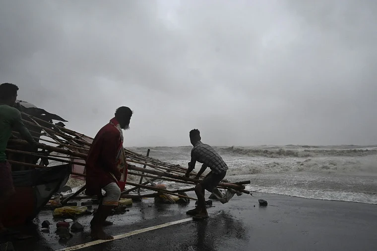 Residents shift structures of makeshifts stalls as water reaches a road at a beachfront area while strong winds batter Balasore district