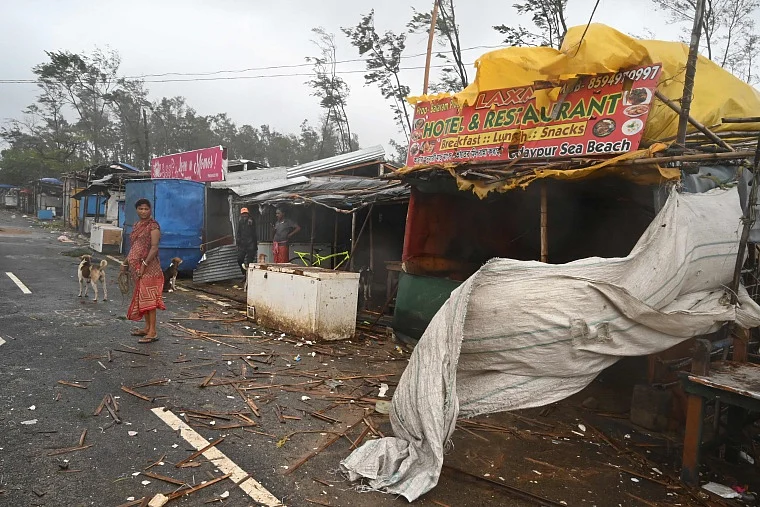 Residents stand near stalls along a road amidst debris while strong winds batter Balasore district