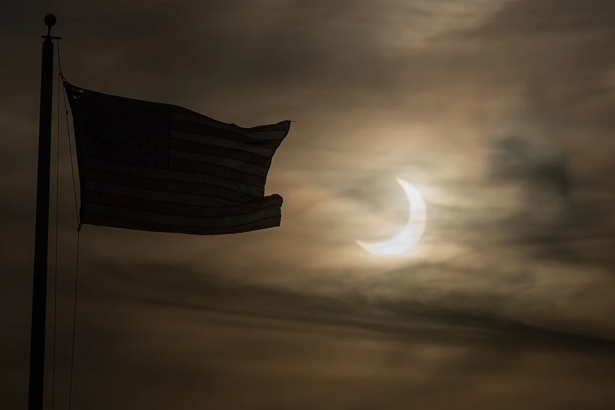 n eclipsed sun rises next to a flag on June 10, 2021 in Scituate, Massachusetts.