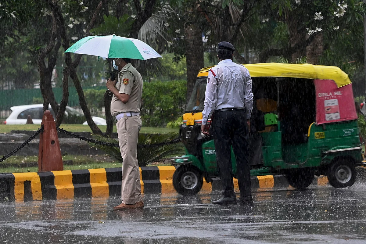 A traffic (R) policeman stands next to a colleague while overseeing traffic along a road during a monsoon rainfall in New Delhi on June 17, 2021.