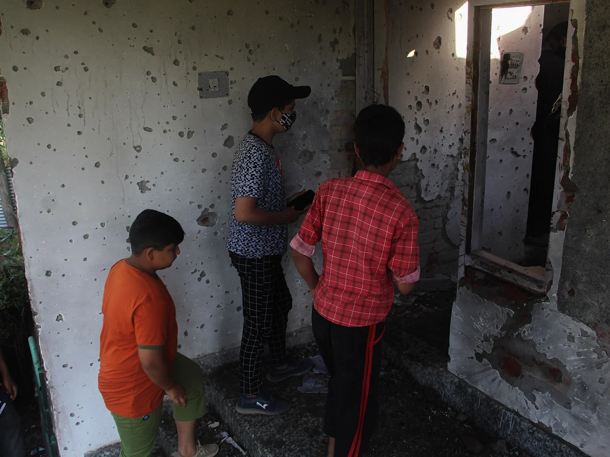 Kashmiri children's stands next to the bullet-ridden wall inside the house that was damaged during a gunfight between security forces and militants in Maloora locality on the outskirts of Srinagar, Jammu & Kashmir.