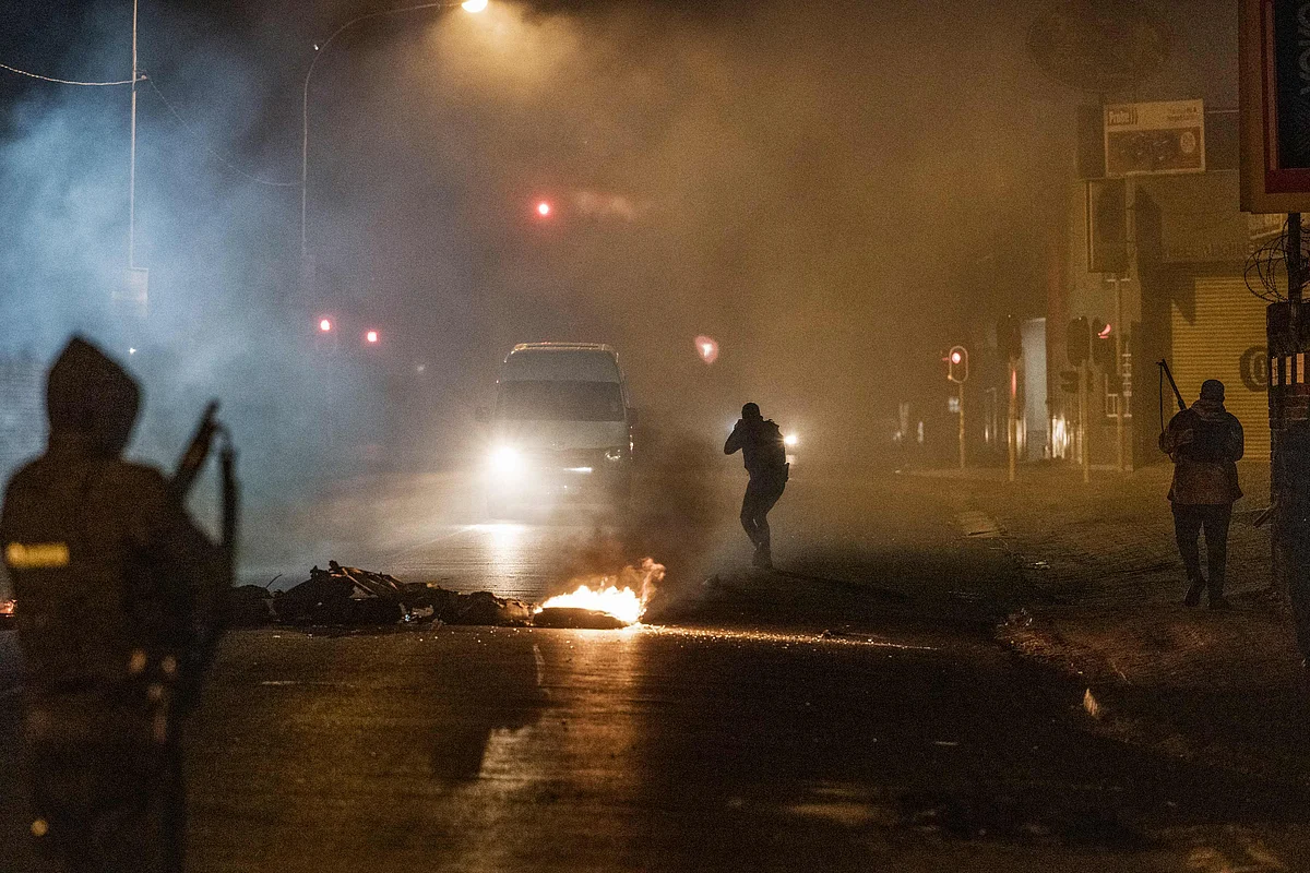 A South Africa Police Service (SAPS) officer aims his rifle at a in incoming minivan bringing it to a stop in Jeppestown, Johannesburg, on July 12, 2021 during clashes with residents of the Wolhuter Mens Hostel.