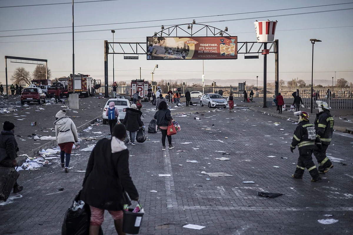 South African firefighters (R) look on as suspected looters walk outside a vandalised mall in Vosloorus, on the outskirts of Johannesburg, on July 14, 2021.
