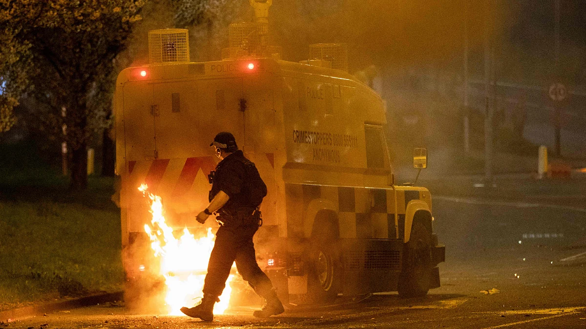 A police officer walks behind a police vehicle with flames leaping up the rear after violence broke out in Newtownabbey, north of Belfast, in Northern Ireland on April 3, 2021