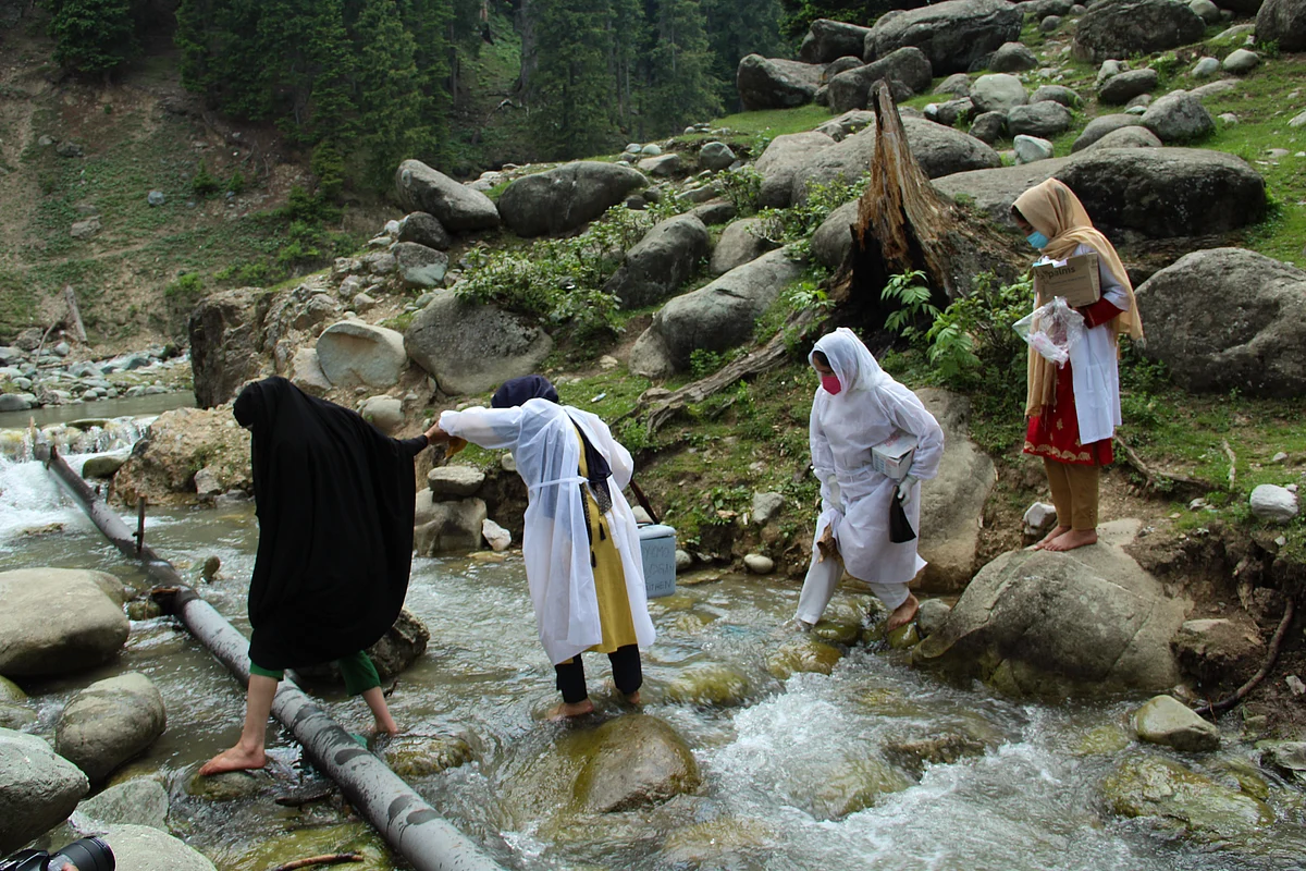 Healthcare workers cross a stream to reach to tge forest area to inoculate nomadic people with a coronavirus disease (COVID-19) vaccine during a vaccination drive in central Kashmir's Budgam district.