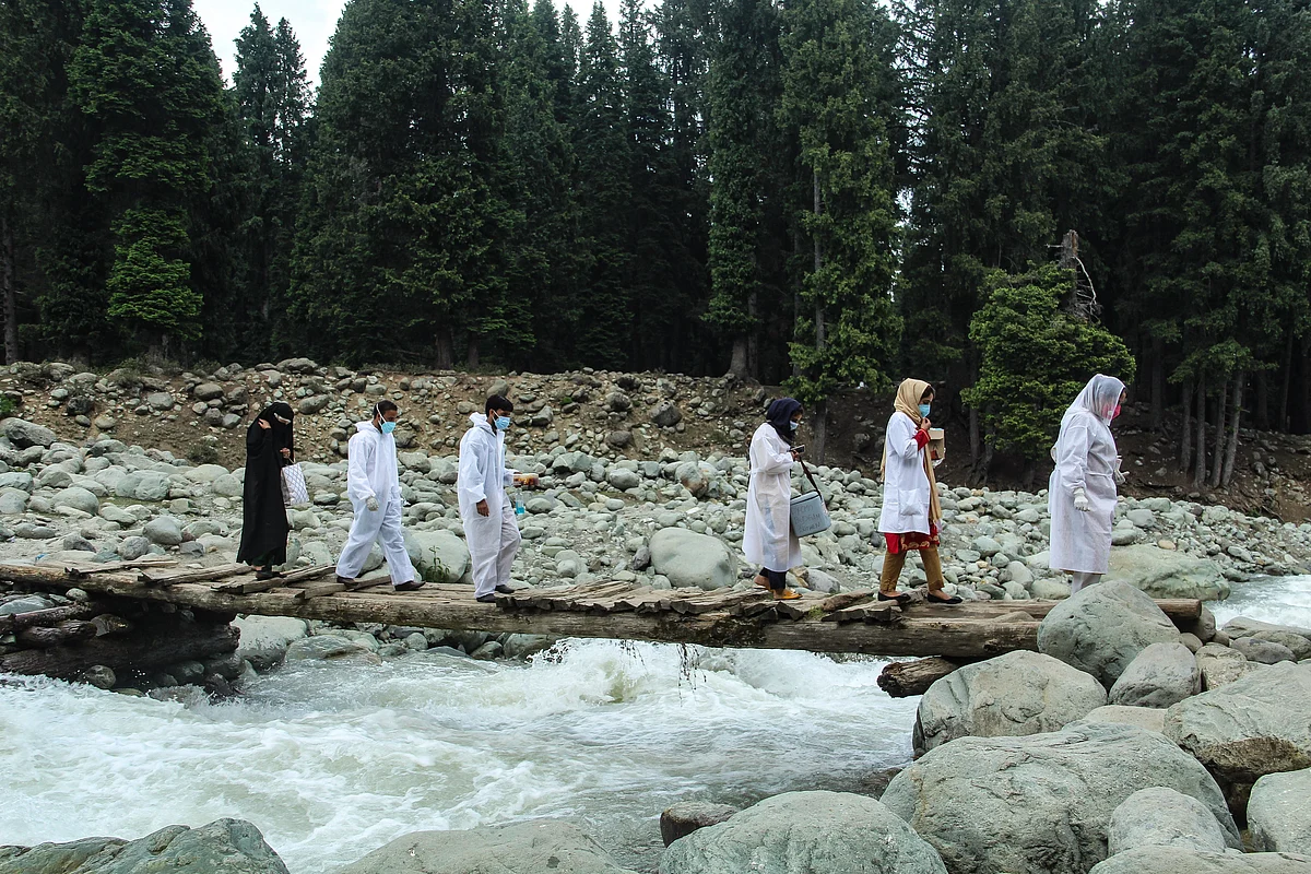 Healthcare workers cross a stream to reach the forest area in central Kashmir's Budgam district to inoculate nomadic with a coronavirus disease (COVID-19) vaccine during a vaccination drive.