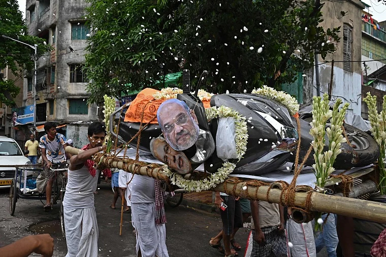 Activists mock a funeral procession of a petrol run vehicle with masks of Indian Prime Minister Narendra Modi and Indian Home Minister Amit Shah during a demonstration to protest against the rising fuel prices along a road in Kolkata