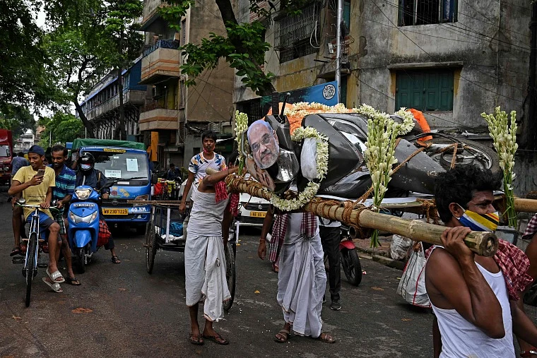 Activists mock a funeral procession of a petrol run vehicle with masks of Indian Prime Minister Narendra Modi and Indian Home Minister Amit Shah during a demonstration to protest against the rising fuel prices along a road in Kolkata